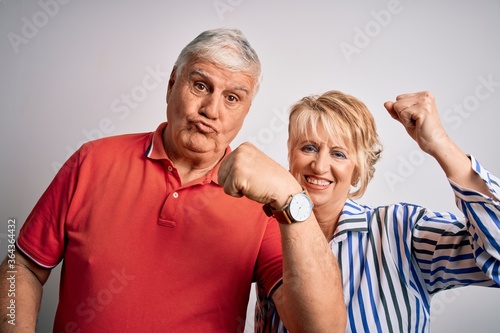 Senior beautiful couple standing together over isolated white background showing arms muscles smiling proud. Fitness concept.