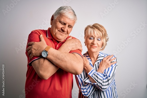 Senior beautiful couple standing together over isolated white background Hugging oneself happy and positive, smiling confident. Self love and self care