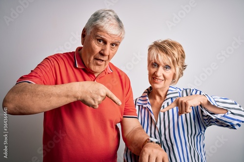 Senior beautiful couple standing together over isolated white background In hurry pointing to watch time, impatience, upset and angry for deadline delay