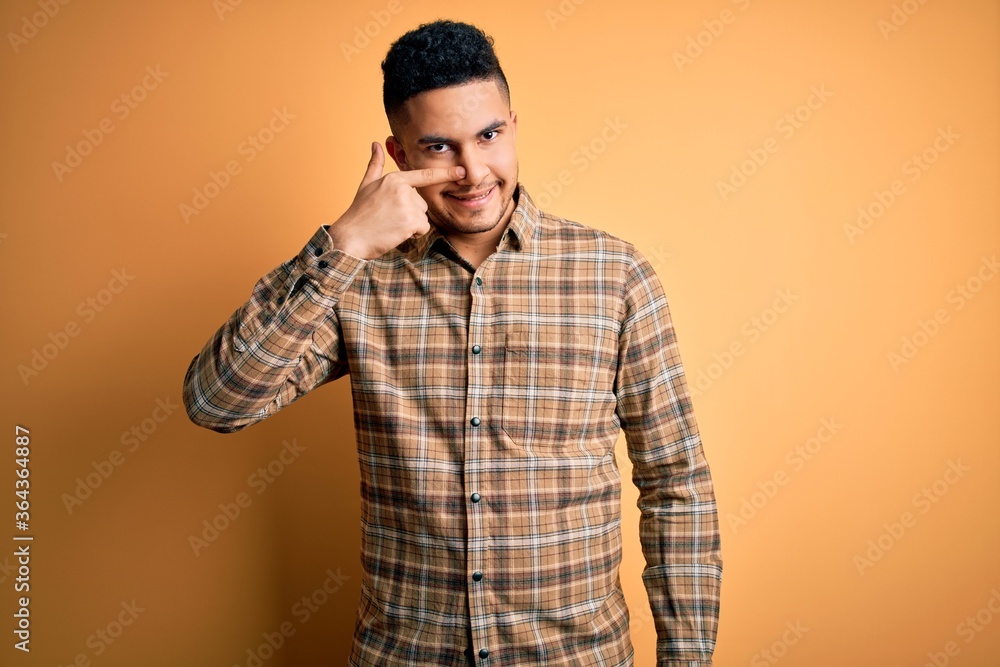 Young handsome man wearing casual shirt standing over isolated yellow background Pointing with hand finger to face and nose, smiling cheerful. Beauty concept