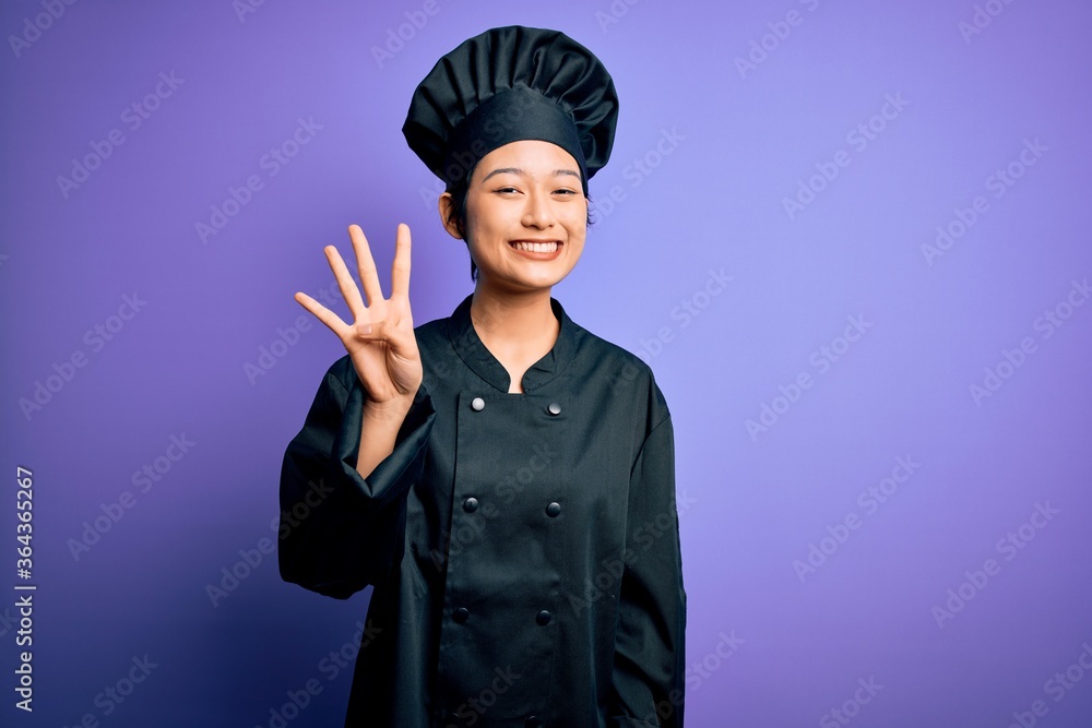 Young beautiful chinese chef woman wearing cooker uniform and hat over purple background showing and pointing up with fingers number four while smiling confident and happy. Young beautiful chinese chef woman wearing cooker uniform and hat over purple background showing and pointing up with fingers number four while smiling confident and happy.