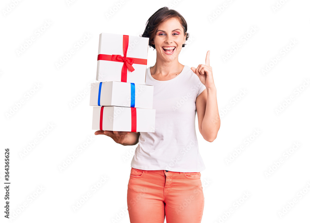 Beautiful young woman with short hair holding gifts surprised with an idea or question pointing finger with happy face, number one Beautiful young woman with short hair holding gifts surprised with an idea or question pointing finger with happy face, number one