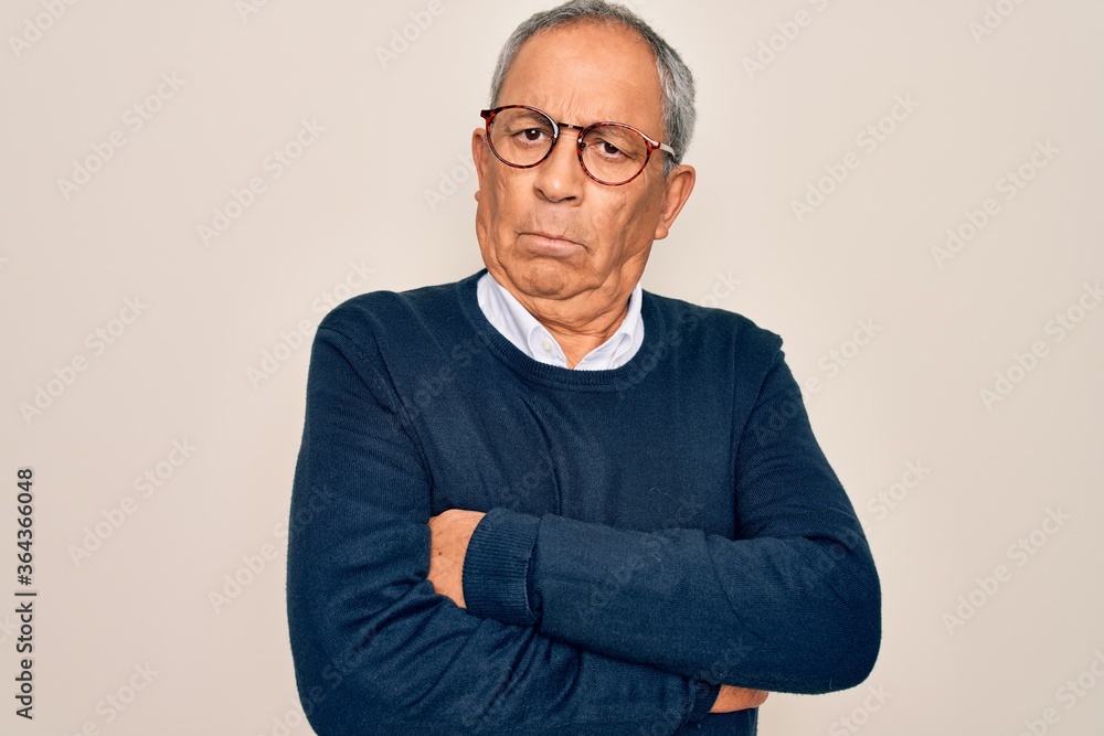 Senior handsome grey-haired man wearing sweater and glasses over isolated white background skeptic and nervous, disapproving expression on face with crossed arms. Negative person. Senior handsome grey-haired man wearing sweater and glasses over isolated white background skeptic and nervous, disapproving expression on face with crossed arms. Negative person.