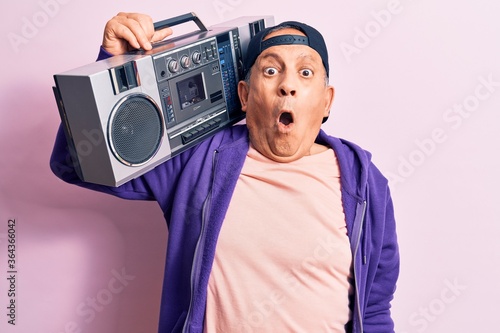 Senior handsome grey-haired modern man listening to music using vintage boombox scared and amazed with open mouth for surprise, disbelief face