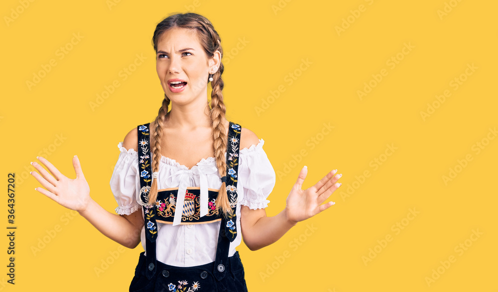 Beautiful caucasian woman with blonde hair wearing octoberfest traditional clothes crazy and mad shouting and yelling with aggressive expression and arms raised. frustration concept. Beautiful caucasian woman with blonde hair wearing octoberfest traditional clothes crazy and mad shouting and yelling with aggressive expression and arms raised. frustration concept.