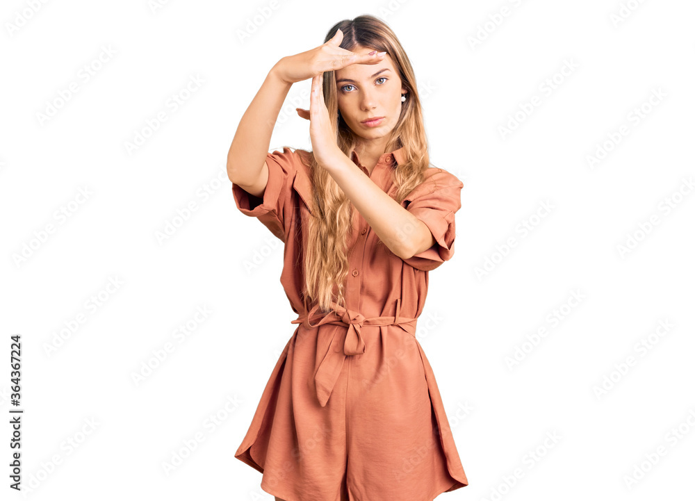 Beautiful caucasian woman with blonde hair wearing summer jumpsuit doing time out gesture with hands, frustrated and serious face