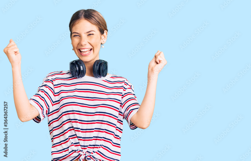 Beautiful caucasian woman with blonde hair wearing gym clothes and using headphones screaming proud, celebrating victory and success very excited with raised arms