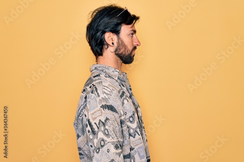 Young handsome hispanic bohemian man wearing hippie style and sunglasses looking to side, relax profile pose with natural face with confident smile.