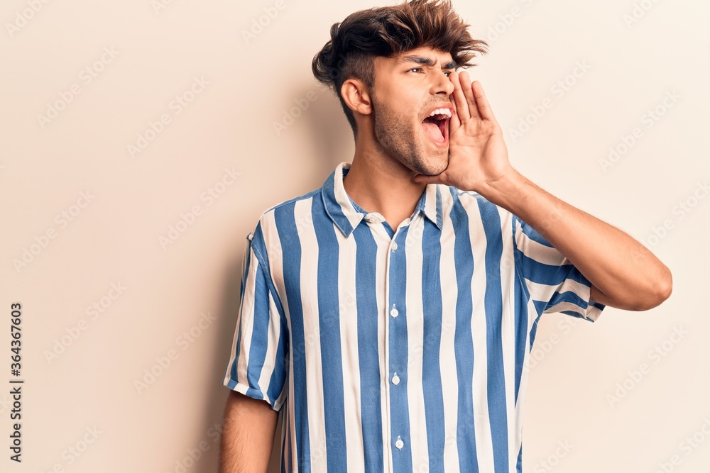 Young hispanic man wearing casual clothes shouting and screaming loud to side with hand on mouth. communication concept. Young hispanic man wearing casual clothes shouting and screaming loud to side with hand on mouth. communication concept.