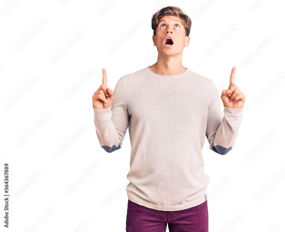 Young handsome man wearing casual clothes amazed and surprised looking up and pointing with fingers and raised arms. Young handsome man wearing casual clothes amazed and surprised looking up and pointing with fingers and raised arms.