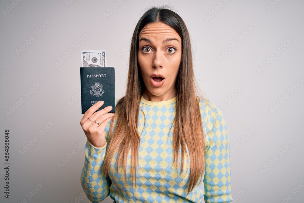 Young blonde tourist woman holding id passport with dollar as money for vacation scared in shock with a surprise face, afraid and excited with fear expression Young blonde tourist woman holding id passport with dollar as money for vacation scared in shock with a surprise face, afraid and excited with fear expression