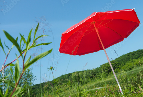 Red sun umbrella on green grass in the background of a small lake  bottom view.