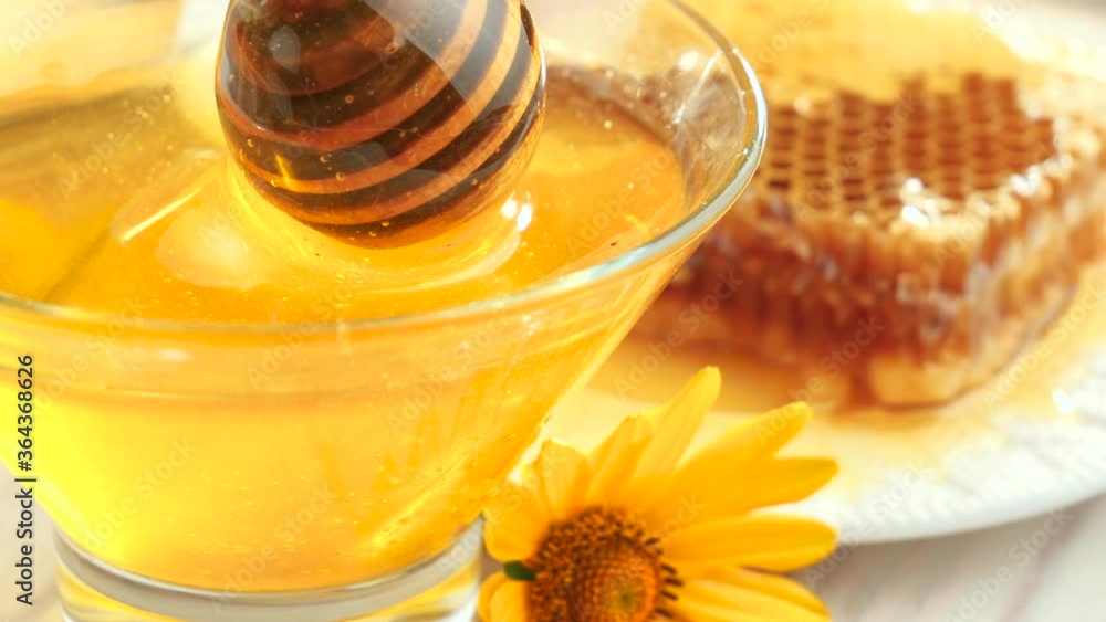 Sweet bee honey is mixed with a honey stick in a glass jar Sweet bee honey is mixed with a honey stick in a glass jar
