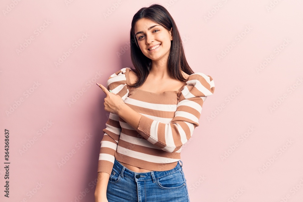 Young beautiful girl wearing casual striped t shirt smiling cheerful pointing with hand and finger up to the side Young beautiful girl wearing casual striped t shirt smiling cheerful pointing with hand and finger up to the side