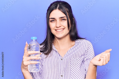 Young beautiful girl holding bottle of water screaming proud, celebrating victory and success very excited with raised arm
