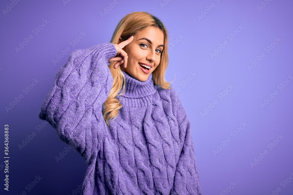 Young beautiful blonde woman wearing casual turtleneck sweater over purple background Smiling pointing to head with one finger, great idea or thought, good memory Young beautiful blonde woman wearing casual turtleneck sweater over purple background Smiling pointing to head with one finger, great idea or thought, good memory