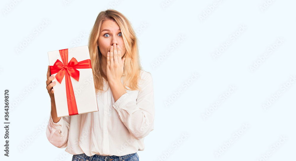Young beautiful blonde woman holding gift with open hand doing stop sign with serious and confident expression, defense gesture Young beautiful blonde woman holding gift with open hand doing stop sign with serious and confident expression, defense gesture
