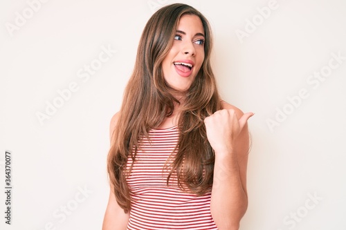 Beautiful young caucasian woman wearing casual clothes smiling with happy face looking and pointing to the side with thumb up.
