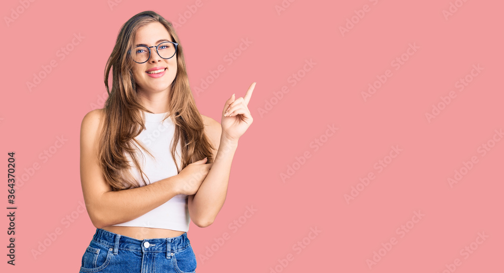 Beautiful caucasian young woman wearing casual clothes and glasses with a big smile on face, pointing with hand and finger to the side looking at the camera. Beautiful caucasian young woman wearing casual clothes and glasses with a big smile on face, pointing with hand and finger to the side looking at the camera.