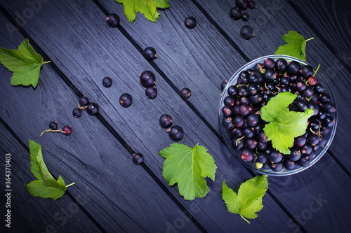 Black currant and green leaves on a dark wooden background. Background with currant berries and green leaves. Currant Macro.