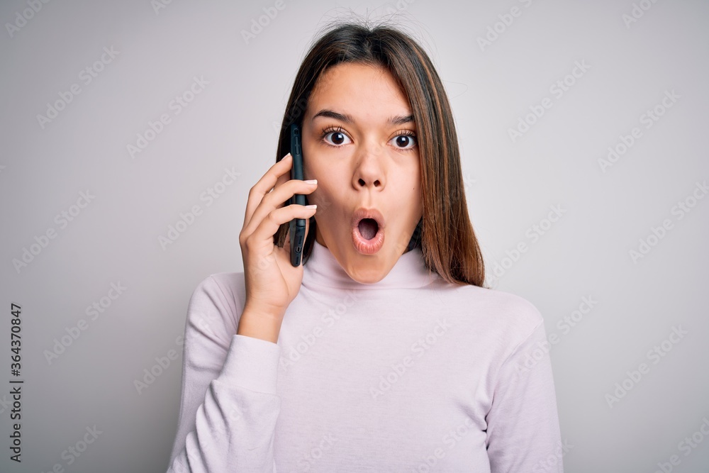Beautiful brunette girl having conversation talking on the smartphone over white background scared in shock with a surprise face, afraid and excited with fear expression Beautiful brunette girl having conversation talking on the smartphone over white background scared in shock with a surprise face, afraid and excited with fear expression