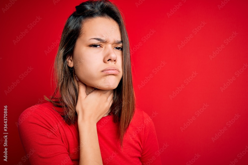 Young beautiful brunette girl wearing casual t-shirt over isolated red background Touching painful neck, sore throat for flu, clod and infection Young beautiful brunette girl wearing casual t-shirt over isolated red background Touching painful neck, sore throat for flu, clod and infection