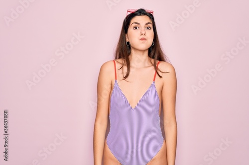 Young beautiful fashion girl wearing swimwear swimsuit and sunglasses over pink background puffing cheeks with funny face. Mouth inflated with air, crazy expression.