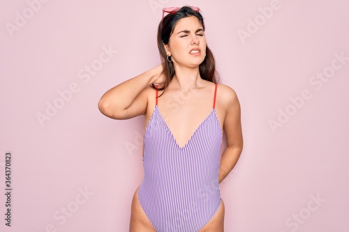 Young beautiful fashion girl wearing swimwear swimsuit and sunglasses over pink background Suffering of neck ache injury  touching neck with hand  muscular pain