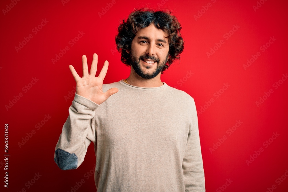 Young handsome man with beard wearing casual sweater standing over red background showing and pointing up with fingers number five while smiling confident and happy. Young handsome man with beard wearing casual sweater standing over red background showing and pointing up with fingers number five while smiling confident and happy.