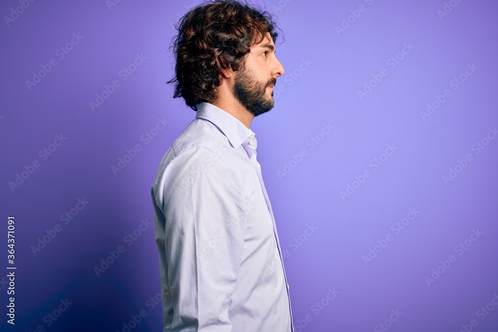 Young handsome business man with beard wearing shirt standing over purple background looking to side, relax profile pose with natural face and confident smile.