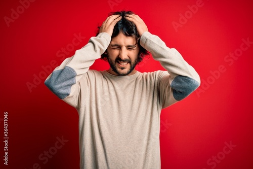 Young handsome man with beard wearing casual sweater standing over red background suffering from headache desperate and stressed because pain and migraine. Hands on head. © Krakenimages.com