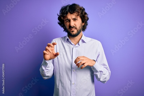 Young handsome business man with beard wearing shirt standing over purple background disgusted expression, displeased and fearful doing disgust face because aversion reaction.