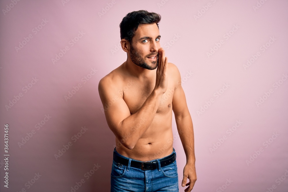 Young handsome strong man with beard shirtless standing over isolated pink background hand on mouth telling secret rumor, whispering malicious talk conversation Young handsome strong man with beard shirtless standing over isolated pink background hand on mouth telling secret rumor, whispering malicious talk conversation