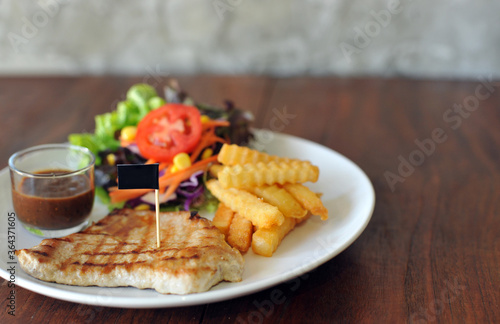 plate of grilled pork steak with french fries and salad on wood background