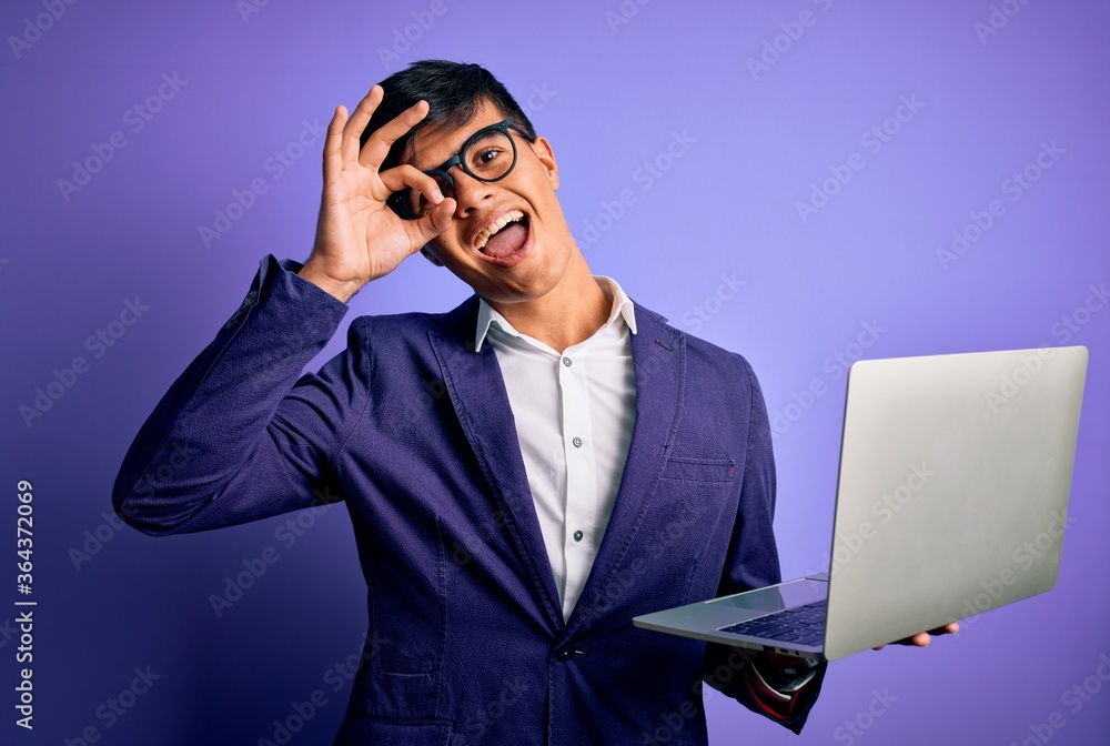Young handsome business man wearing glasses working using laptop over purple background with happy face smiling doing ok sign with hand on eye looking through fingers Young handsome business man wearing glasses working using laptop over purple background with happy face smiling doing ok sign with hand on eye looking through fingers