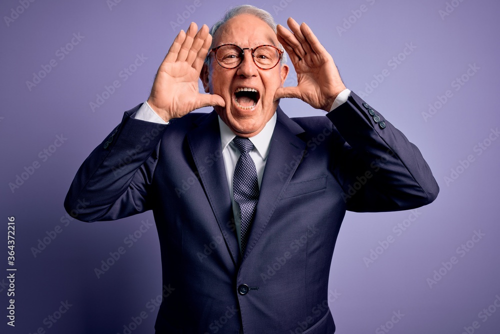 Grey haired senior business man wearing glasses and elegant suit and tie over purple background Smiling cheerful playing peek a boo with hands showing face. Surprised and exited Grey haired senior business man wearing glasses and elegant suit and tie over purple background Smiling cheerful playing peek a boo with hands showing face. Surprised and exited
