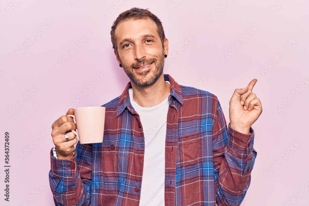 Young handsome man holding coffee smiling happy pointing with hand and finger to the side Young handsome man holding coffee smiling happy pointing with hand and finger to the side