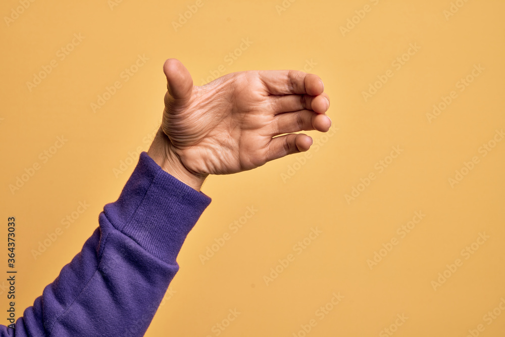 Hand of caucasian young man showing fingers over isolated yellow background holding invisible object, empty hand doing clipping and grabbing gesture