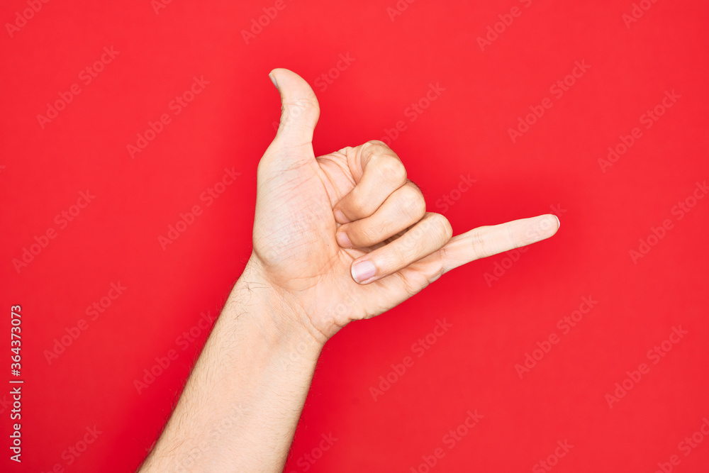 Hand of caucasian young man showing fingers over isolated red background gesturing Hawaiian shaka greeting gesture, telephone and communication symbol