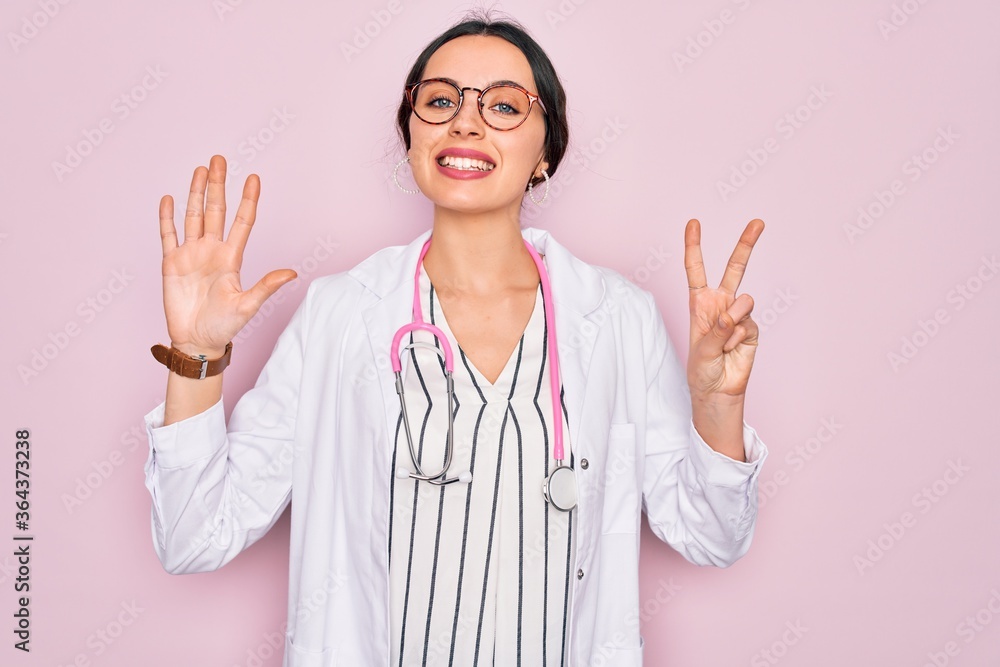 Beautiful doctor woman with blue eyes wearing coat and stethoscope over pink background showing and pointing up with fingers number seven while smiling confident and happy. Beautiful doctor woman with blue eyes wearing coat and stethoscope over pink background showing and pointing up with fingers number seven while smiling confident and happy.