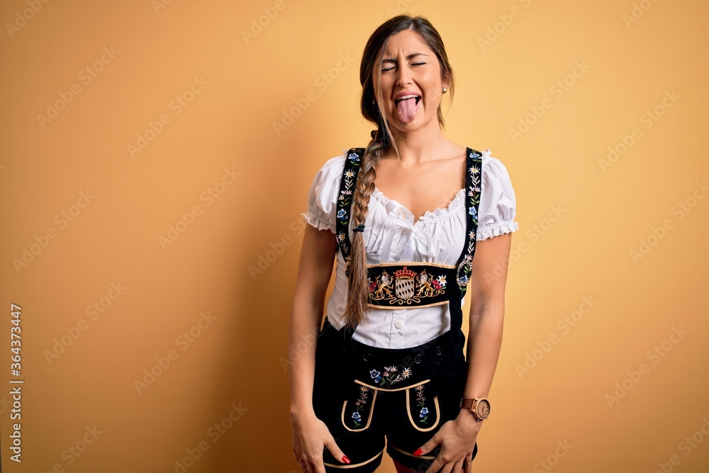 Young beautiful brunette german woman celebrating Octoberfest wearing traditional dress sticking tongue out happy with funny expression. Emotion concept. Young beautiful brunette german woman celebrating Octoberfest wearing traditional dress sticking tongue out happy with funny expression. Emotion concept.
