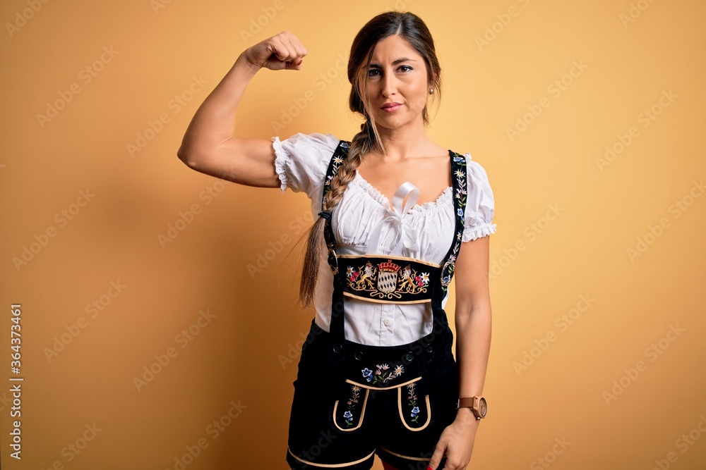 Young beautiful brunette german woman celebrating Octoberfest wearing traditional dress Strong person showing arm muscle, confident and proud of power Young beautiful brunette german woman celebrating Octoberfest wearing traditional dress Strong person showing arm muscle, confident and proud of power