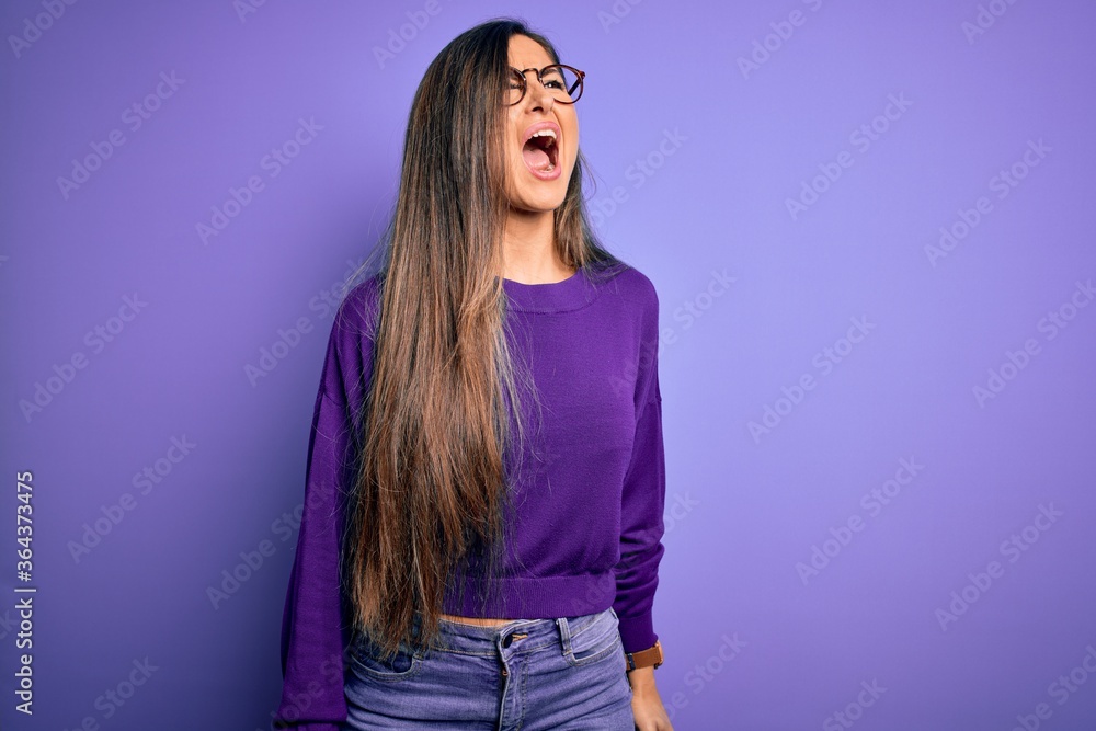 Young beautiful smart woman wearing glasses over purple isolated background angry and mad screaming frustrated and furious, shouting with anger. Rage and aggressive concept.