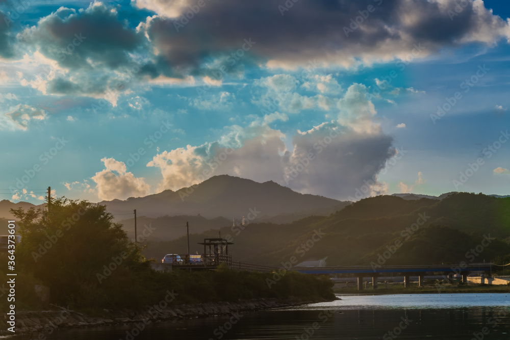 Samcheok, South Korea; September 24, 2018: Dramatic blue cloudy sky over  coastal water inlet at blue hour with bridge and mountains in background.