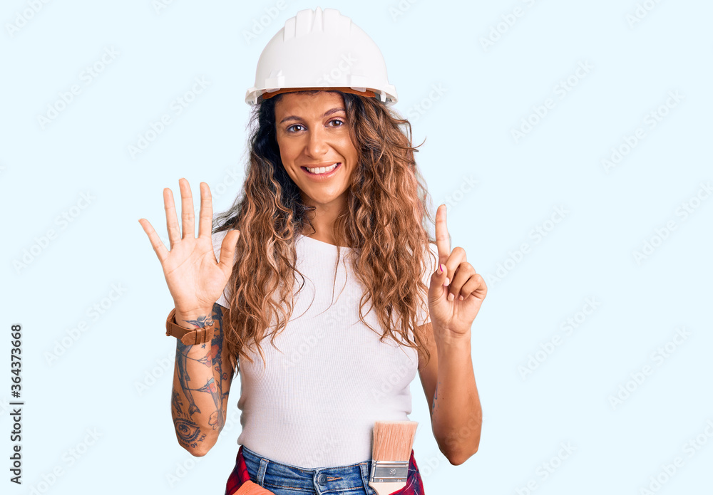 Young hispanic woman with tattoo wearing hardhat and builder clothes showing and pointing up with fingers number six while smiling confident and happy. Young hispanic woman with tattoo wearing hardhat and builder clothes showing and pointing up with fingers number six while smiling confident and happy.
