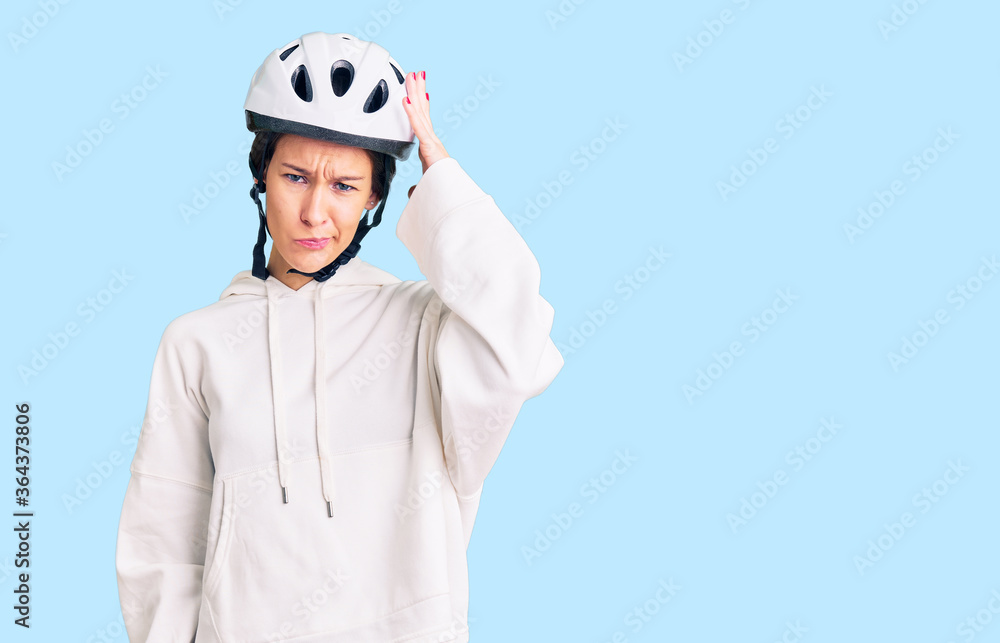 Beautiful brunette young woman wearing bike helmet and sporty clothes confuse and wonder about question. uncertain with doubt, thinking with hand on head. pensive concept. Beautiful brunette young woman wearing bike helmet and sporty clothes confuse and wonder about question. uncertain with doubt, thinking with hand on head. pensive concept.