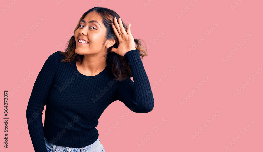 Young beautiful mixed race woman wearing casual clothes smiling with hand over ear listening an hearing to rumor or gossip. deafness concept. Young beautiful mixed race woman wearing casual clothes smiling with hand over ear listening an hearing to rumor or gossip. deafness concept.