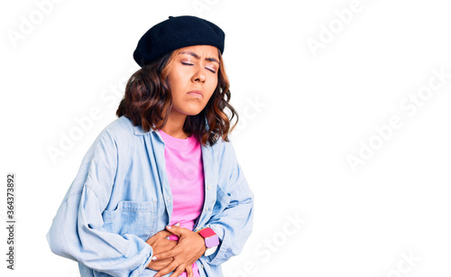 Young beautiful mixed race woman wearing french look with beret with hand on stomach because indigestion, painful illness feeling unwell. ache concept.