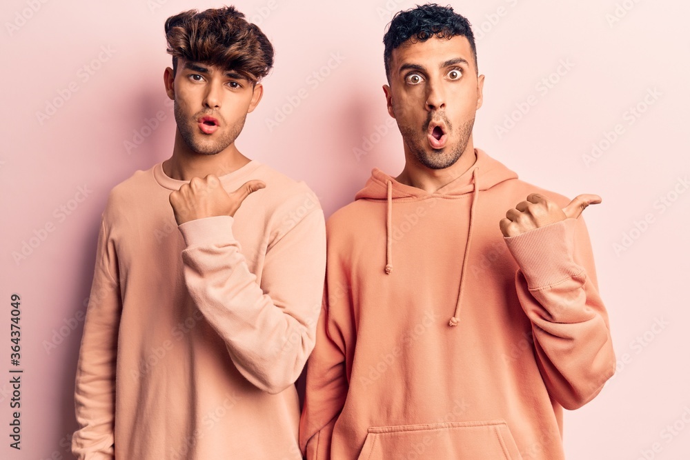 Young gay couple wearing casual clothes surprised pointing with hand finger to the side, open mouth amazed expression. Young gay couple wearing casual clothes surprised pointing with hand finger to the side, open mouth amazed expression.
