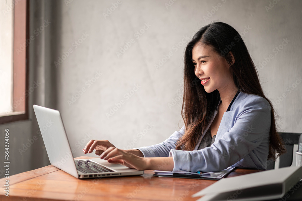 Young happy Asian businesswoman in blue shirt working from home and use a computer laptop and thinking idea for her business Young happy Asian businesswoman in blue shirt working from home and use a computer laptop and thinking idea for her business